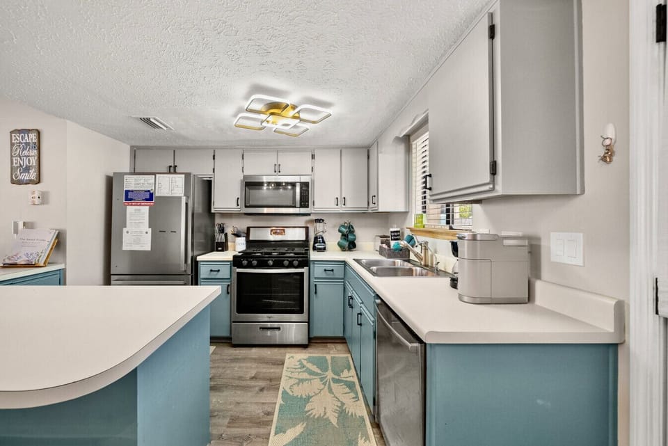 Fully equipped kitchen with stainless appliances, modern lighting, and coastal blue cabinetry