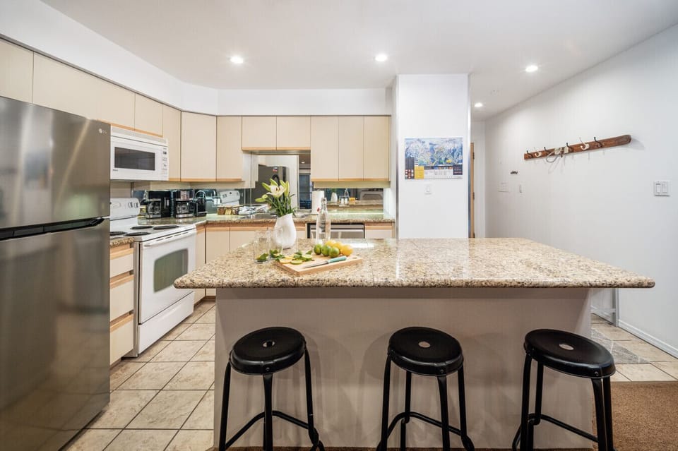 Bright, open kitchen with stainless steel appliances, granite countertops, and a large island with bar seating. Includes a Nespresso machine with pods provided, and flows seamlessly into the living and dining areas.