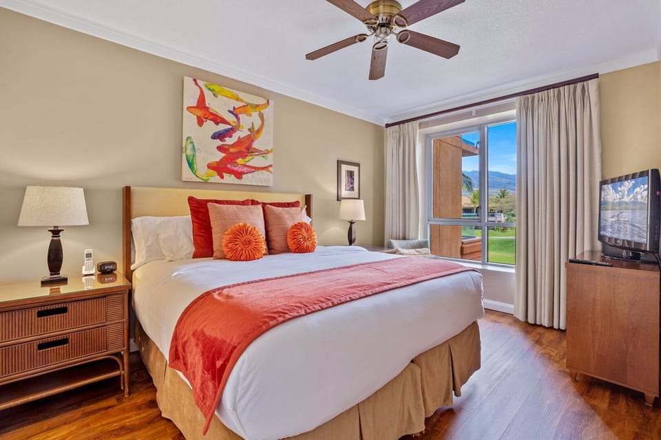 A spacious Guest Suite featuring a comfortable King size bed, vibrant orange accents, and a large window offering peaceful views of the surrounding greenery.
