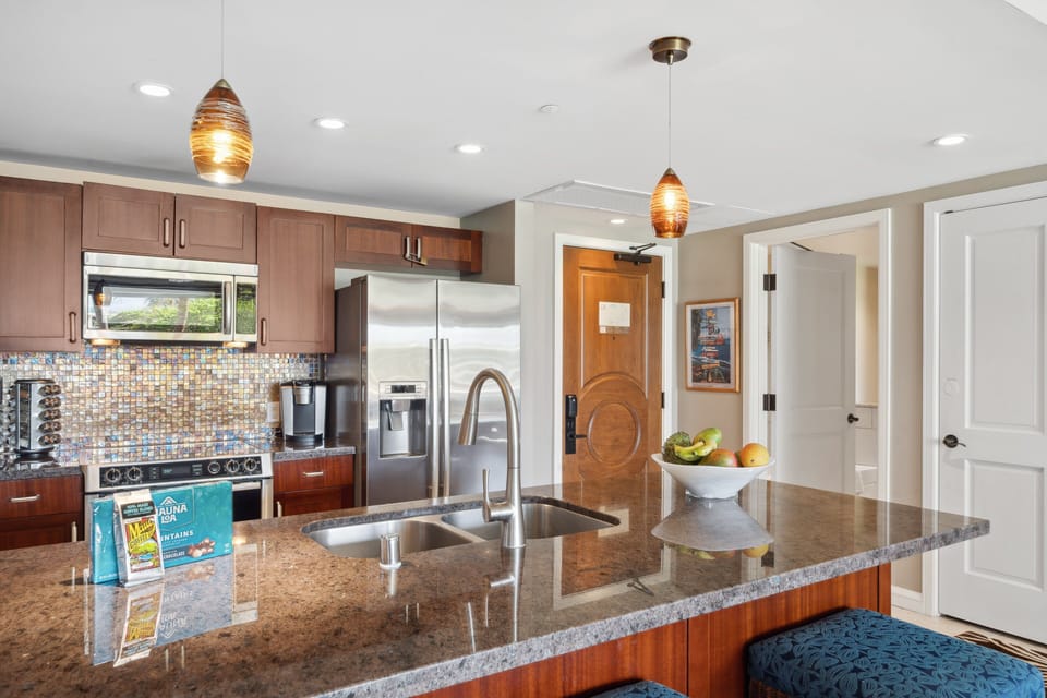 Modern kitchen with a granite island, cushioned bar stools, stainless steel appliances, and stylish pendant lighting.