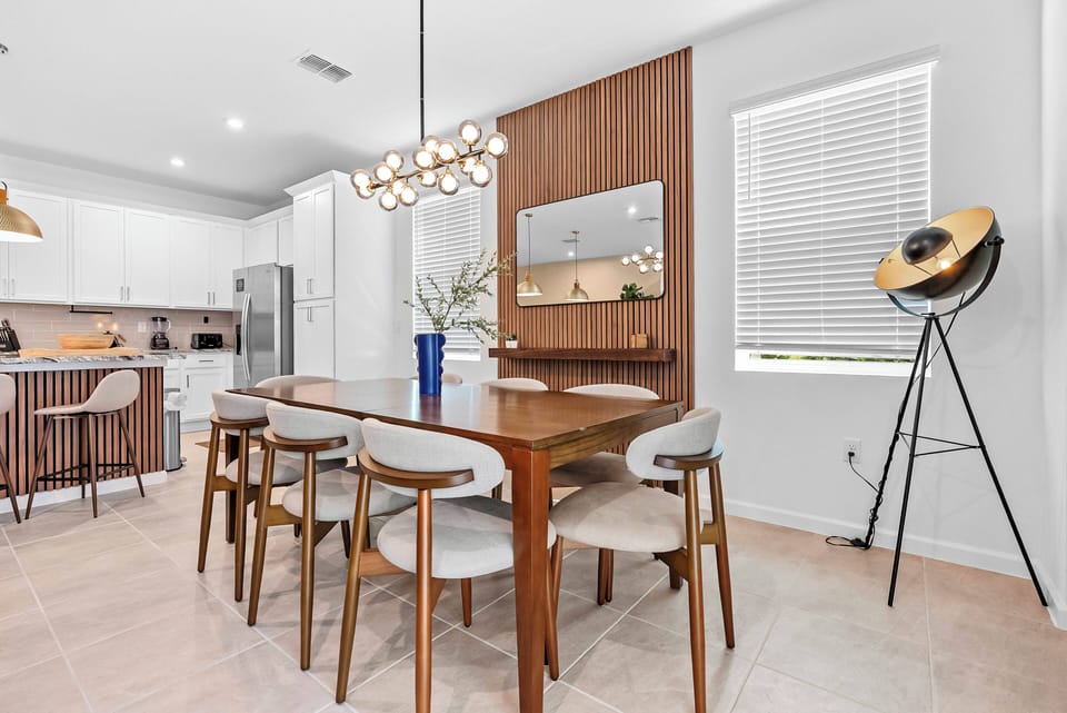 Experience a bright and airy dining area with a beautiful wooden table and sleek upholstered chairs, creating an inviting ambiance. A modern light fixture adds warmth, while playful decor enhances the charm. Enjoy meals in style!