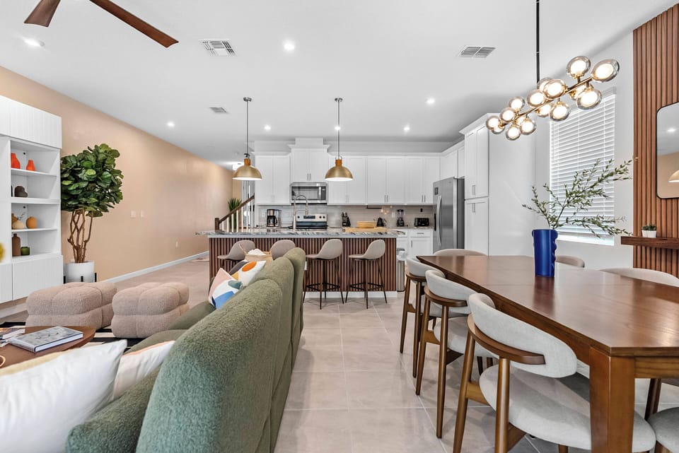 Enjoy a perfect mix of comfort and style in this open living area, complete with a cozy green sofa, stylish pendant lighting, and a inviting dining table, all set in warm tones for a welcoming atmosphere perfect for relaxation.