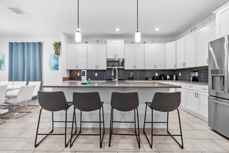 Discover a stylish kitchen that blends elegance and functionality, complete with a spacious island and modern seating. Bright white cabinetry contrasts beautifully with dark tiles, while pendant lighting creates a warm ambiance.