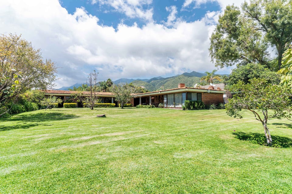 An open grassy expanse sits between the house and the surrounding hills, offering a peaceful view