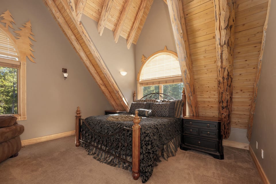 Rest peacefully in this cozy loft bedroom with rustic log beams, soft natural light, and charming forest views.