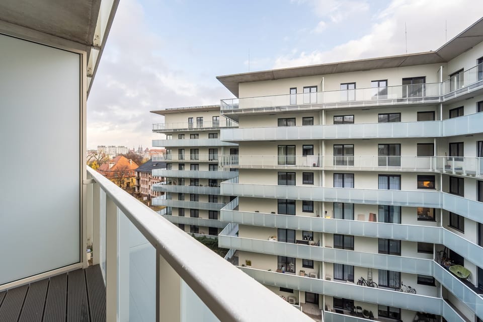 A similar balcony view featuring nearby apartment buildings and open sky. The atmosphere feels calm and urban.