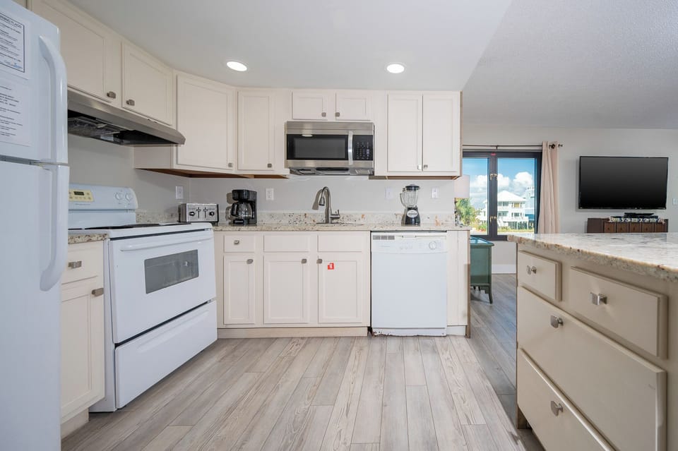 This kitchen features granite countertops, stainless appliances, and a view of the beach from the adjacent living area