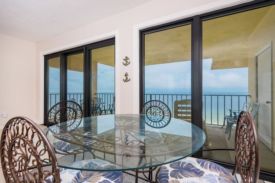 This dining area features a glass table with decorative chairs, offering a lovely view of the tranquil beach