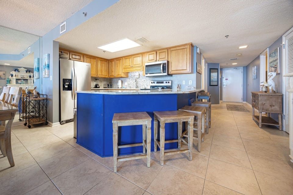 Bright kitchen area features a blue bar with seating, wooden cabinets, and a stylish dining space for casual meals