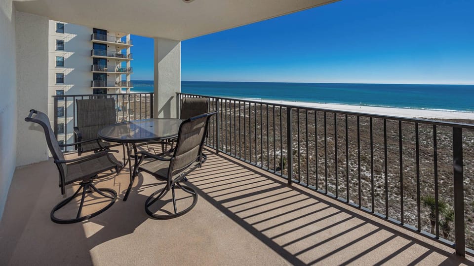 Balcony with a glass-top table and chairs offers a serene view of the gulf and white sand beach, perfect for relaxation