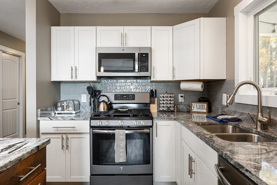 Sleek kitchen w/ stainless steel appliances, granite counters & blue-gray tile backsplash for easy meals.