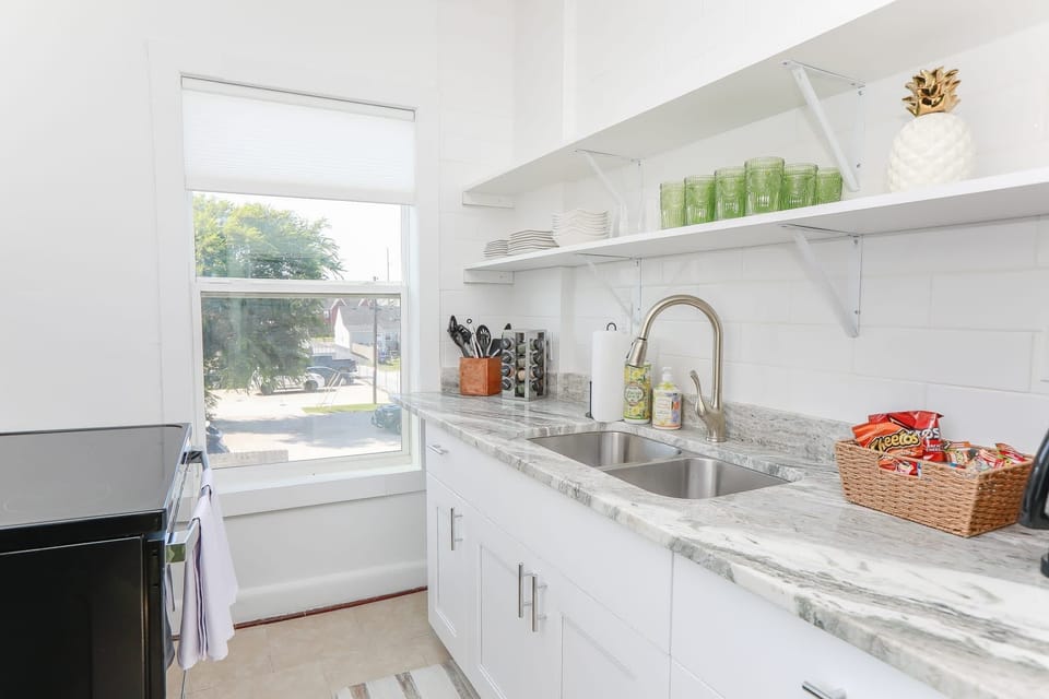 View of dual kitchen sink with kitchenware and spacious overhead shelves.