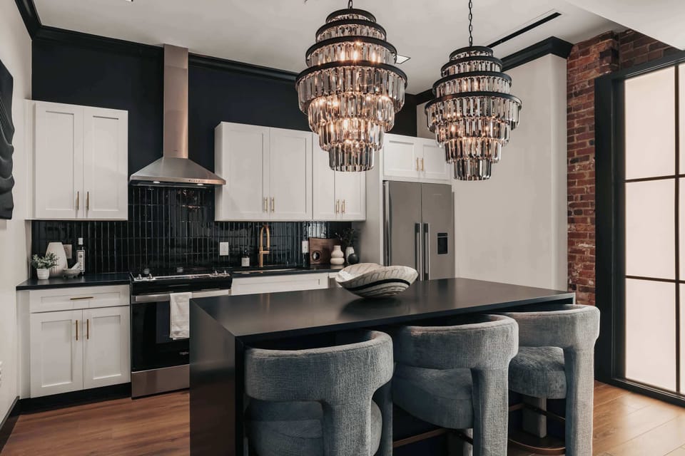 The Highball - The modern kitchen features smoky accents and mirrored finishes, highlighted by stunning glass chandeliers and comfortable bar stools at the island—blending style and function effortlessly.
