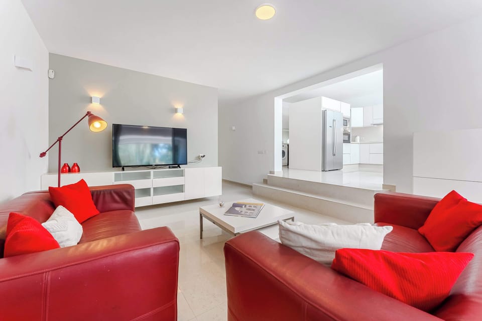 Lounge Area with Bold Red Sofas, Smart TV and Open Flow into Kitchen – Designed for Social Comfort