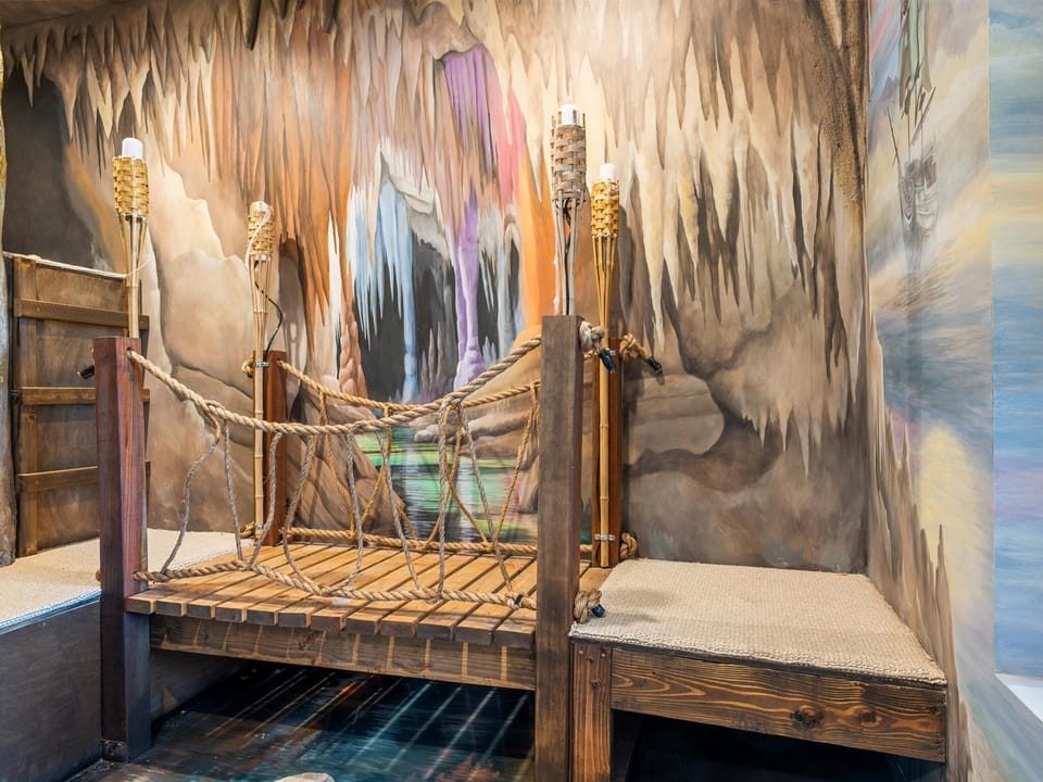 Step into your own adventure with an imaginative cave-themed bedroom featuring a whimsical rope bridge bed, hand-painted stalactite walls, and torchlight ambiance that transforms bedtime into an unforgettable journey.
