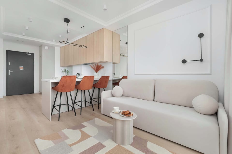 Bright living room with a large window, neutral-toned sofa, and light wooden flooring.
