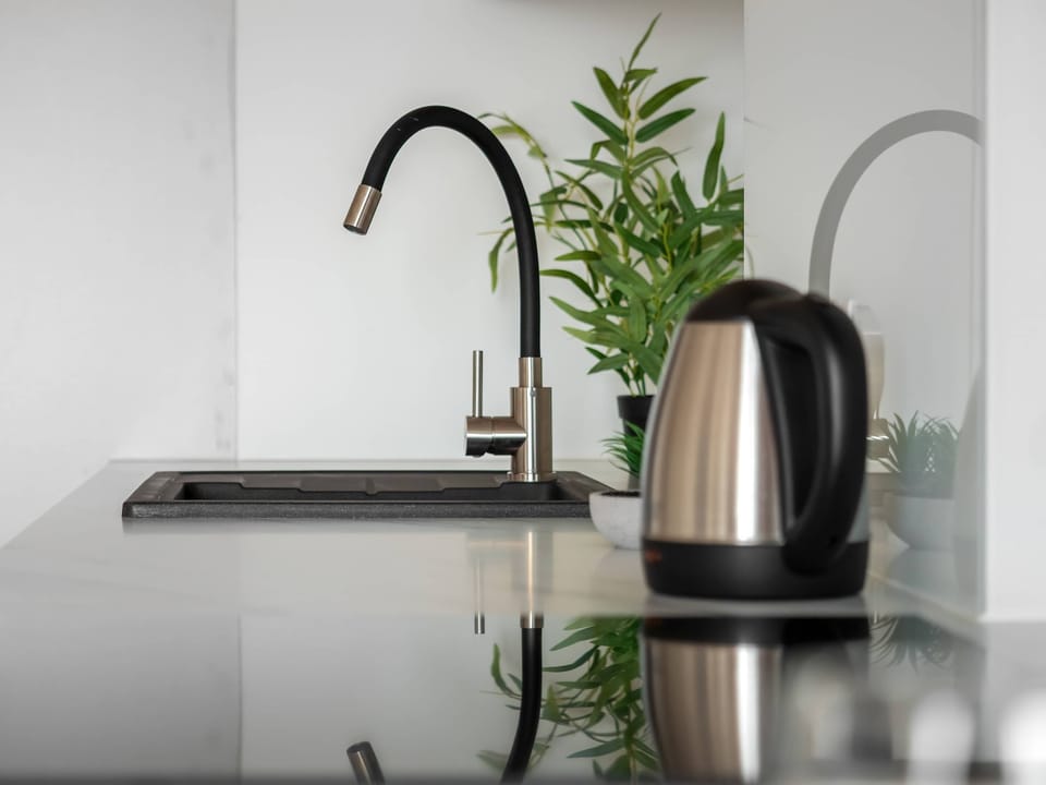 Close-up of kitchen sink with black faucet and stainless-steel kettle.