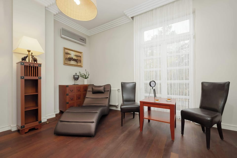 A comfortable bedroom with sitting chairs and a reading lamp by the window. The wooden furniture and soft lighting make it feel inviting.