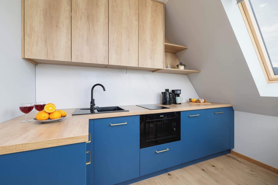 A compact kitchen corner featuring blue lower cabinets, a wooden countertop, and built-in appliances.