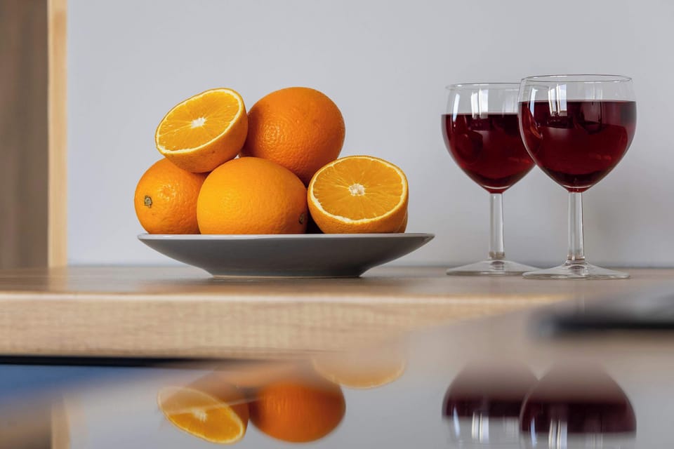A wooden kitchen counter with fresh oranges and two glasses of red juice or wine placed neatly side by side.