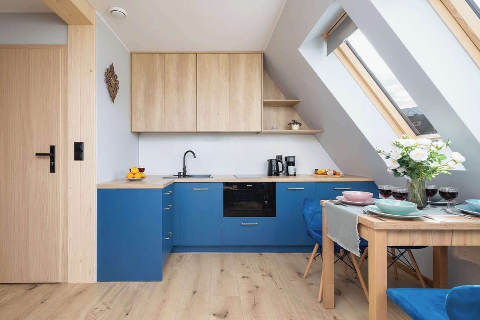 A modern open-plan kitchen with blue cabinets, light wood finishes, and large skylight windows.