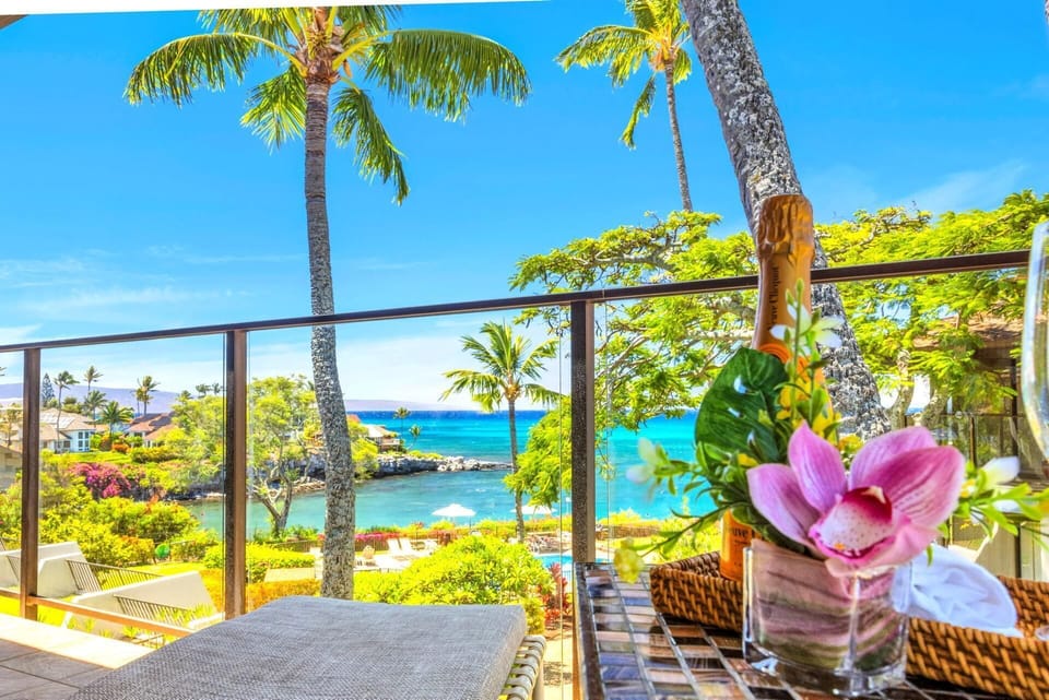 Stunning ocean-view lanai with lush tropical scenery, swaying palms, and a sparkling blue bay — perfect for enjoying a glass of champagne in paradise. NAP-C37