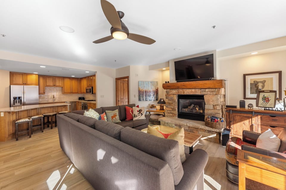 Unwind in your spacious living room with cozy stone fireplace, modern kitchen, and warm wood accents creating the perfect mountain retreat atmosphere.