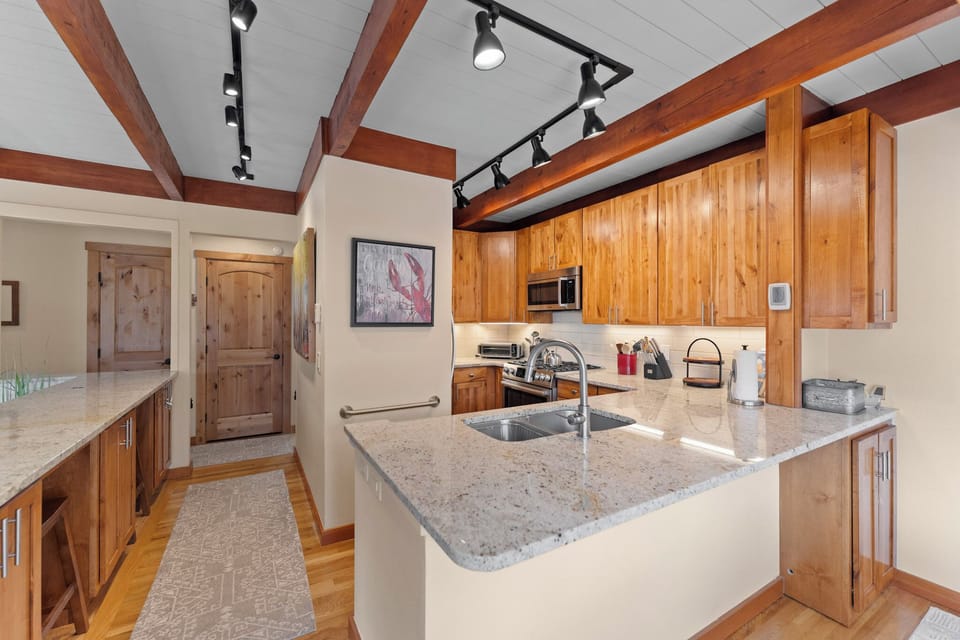 Cook with mountain charm in this elegant kitchen featuring warm wood cabinetry, granite counters, and rustic exposed beams overhead.