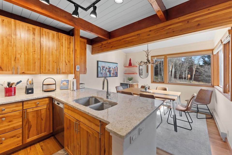 Your modern kitchen features warm wood cabinetry and granite counters, perfect for preparing meals while enjoying forest views through large windows.