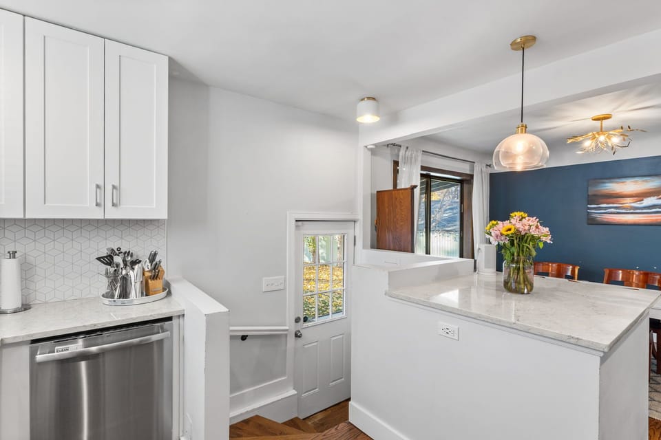 Step into your bright, modern kitchen where crisp white cabinetry meets elegant marble countertops. Fresh flowers await your arrival on the spacious island, while natural light streams through charming windows.