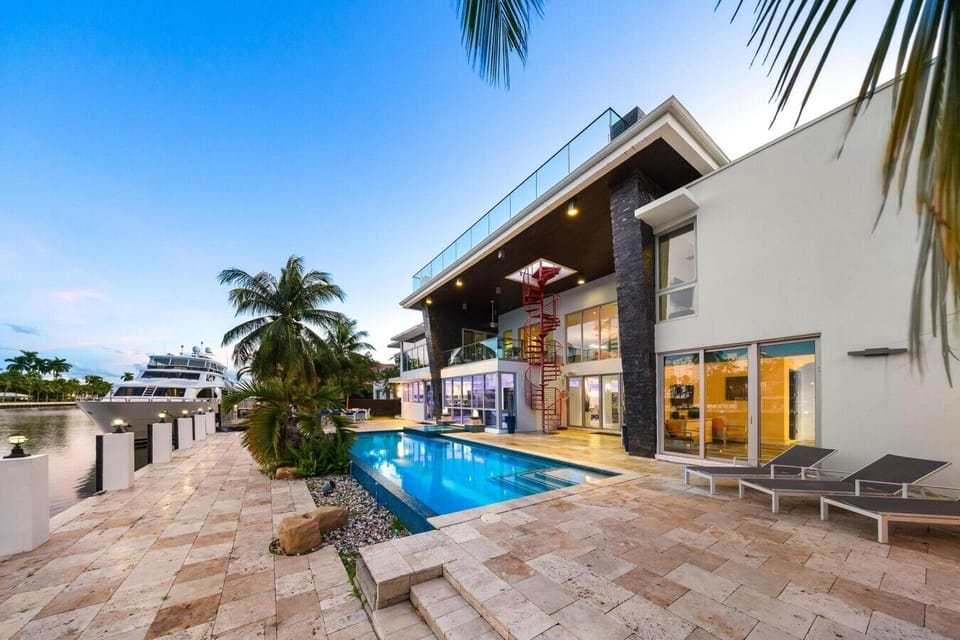 A contemporary multi-level home featuring large floor-to-ceiling windows, glass balconies, and a striking red spiral staircase leading to the upper deck