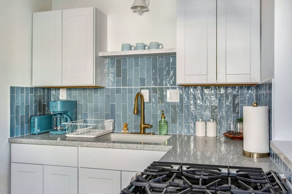 Fully equipped kitchen with stainless steel appliances, cookware, and blue tile backsplash.