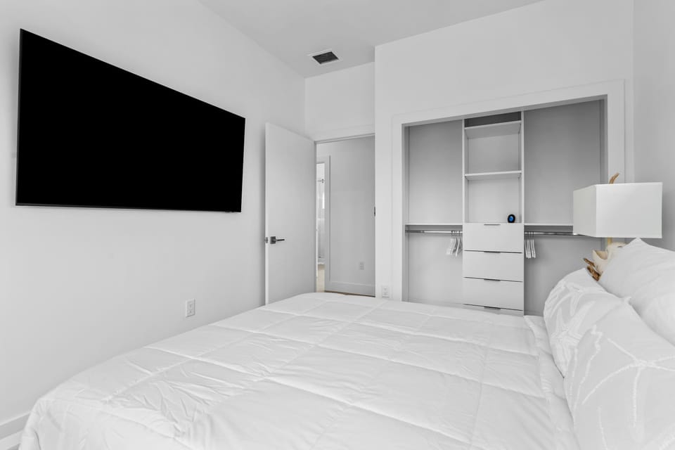 Bright minimalist bedroom with a large smart TV and built-in closet storage