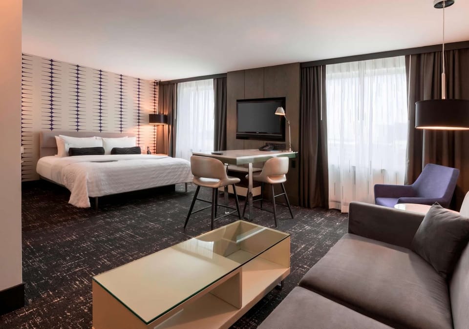 Spacious room with king bed, sofa, TV, and two tall windows