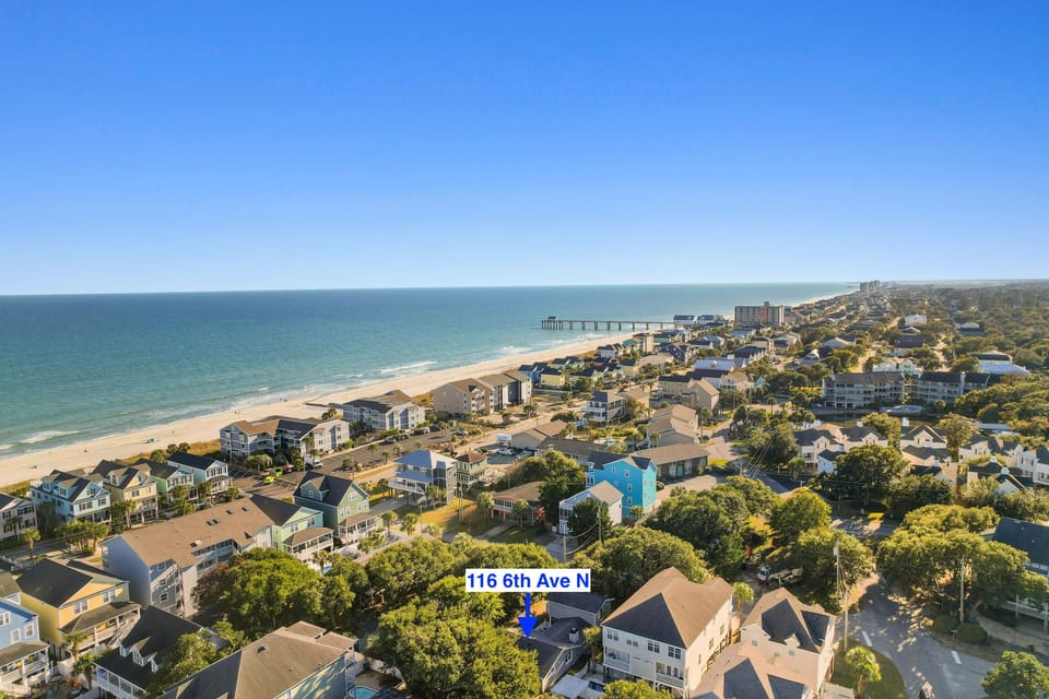 Aerial view showcasing the coastal neighborhood with beach access and tree-lined streets surrounding the property location.
