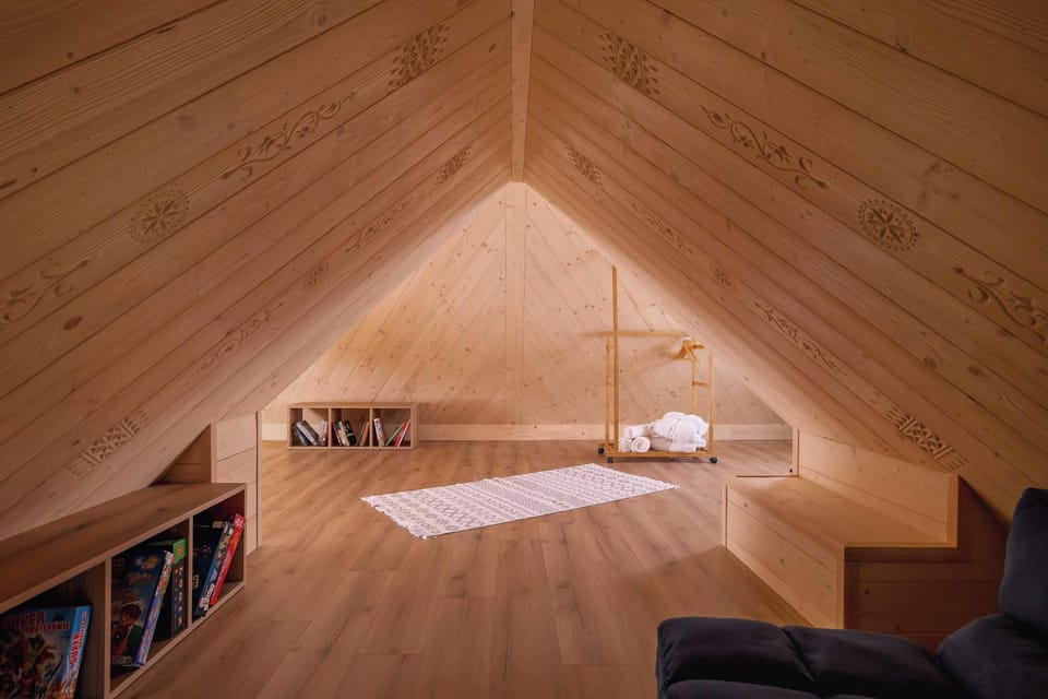 A minimalist attic room with light wooden panels and a comfortable mattress on the floor. The triangular architecture gives it a unique charm.