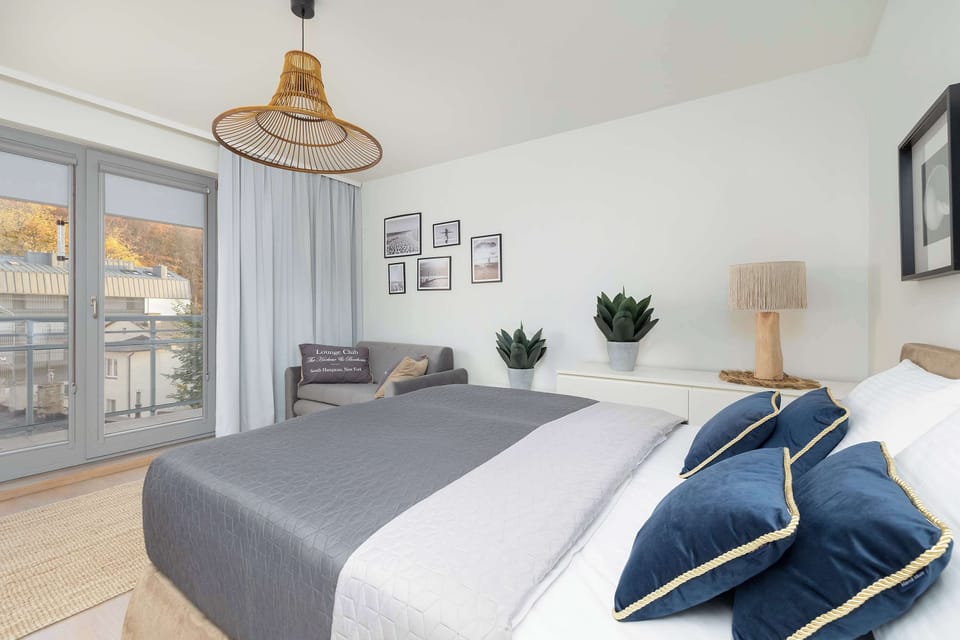 A bright bedroom with a bed, large windows, and houseplants adding freshness.