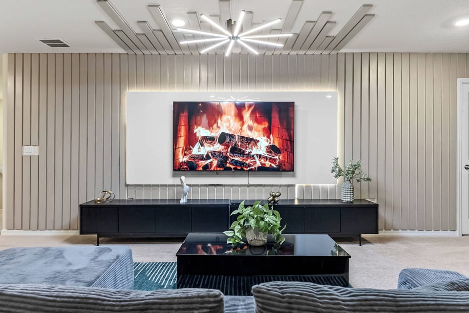 Unwind in a stylish living area with a sleek black media console and a cozy electric fireplace that enhance the chic decor. A stunning starburst chandelier brightens the textured walls, creating an inviting atmosphere just for.