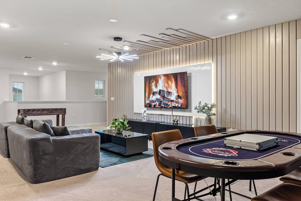 Enjoy a cozy living area with a plush gray sofa and a captivating feature wall lit for relaxation. The stylish poker table invites friendly competition, perfect for fun evenings in a comfortable setting.