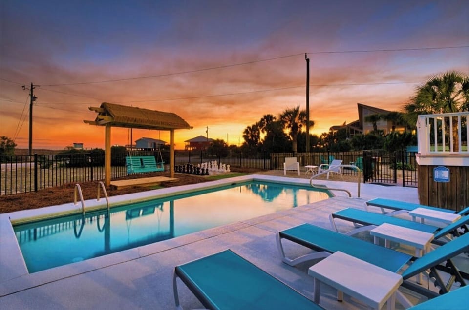 Stunning sunset paints the sky over this tropical pool area with palm trees and comfortable loungers for evening relaxation.