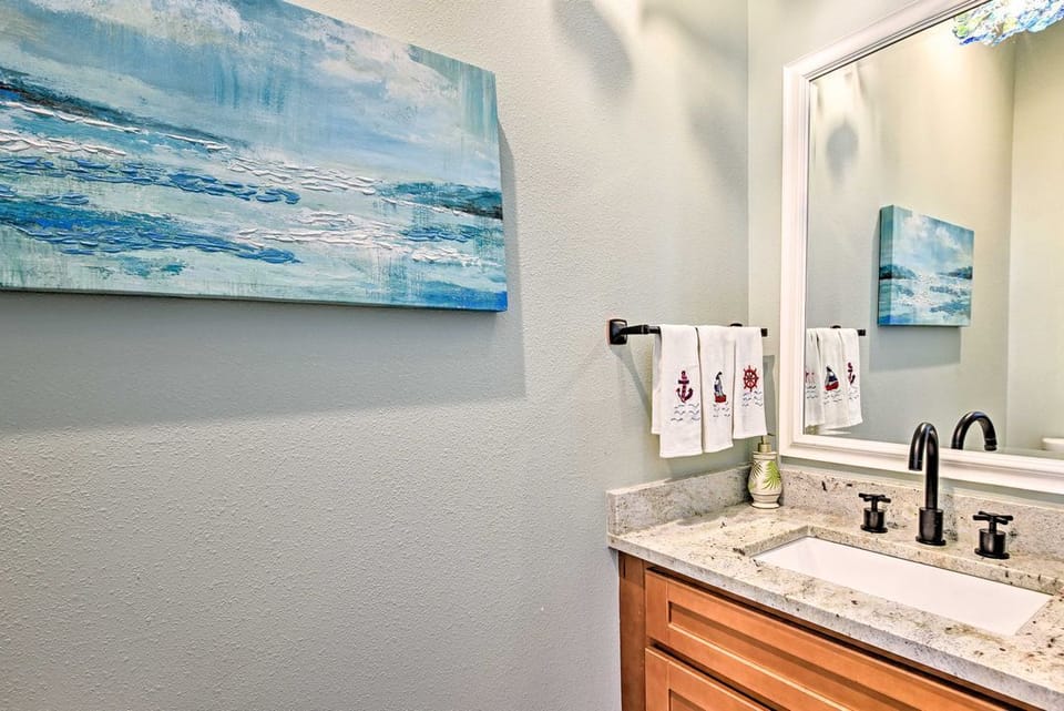 Bathroom vanity with stone countertop, dark fixtures, and coastal wall art.