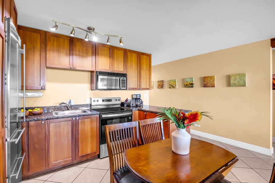 Cook and gather in a well-equipped kitchen showcasing rich wood cabinetry, stainless-steel appliances, and a cozy dining area accented with a fresh floral centerpiece.