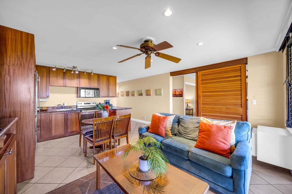 Gather in a bright living space featuring a plush sofa with colorful pillows, warm wood accents, and an open layout that flows seamlessly into a fully equipped kitchen and dining area.