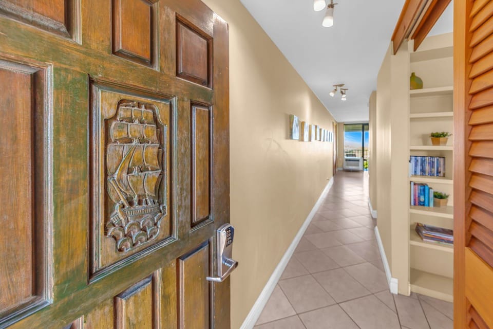 Enter through a charming wooden door with intricate carvings into a welcoming hallway lined with built-in shelving and tasteful artwork.