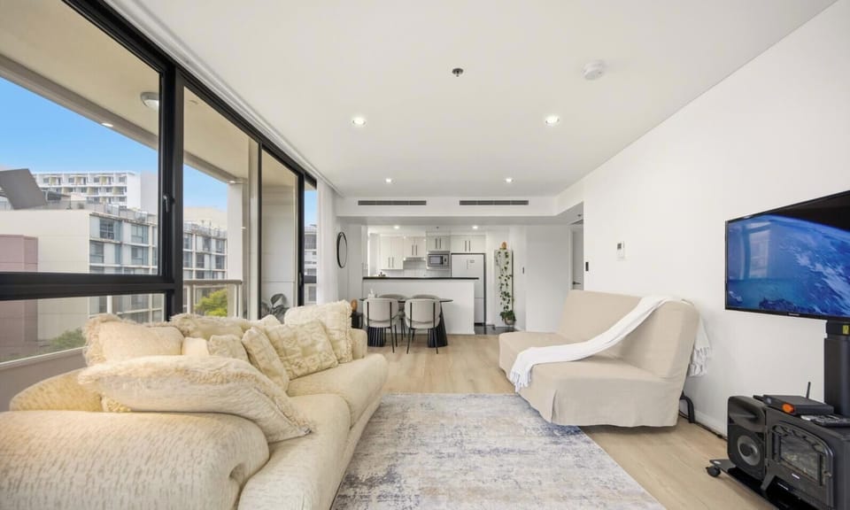 An open-plan living space with a large sofa and a television set, overlooking an outdoor area.