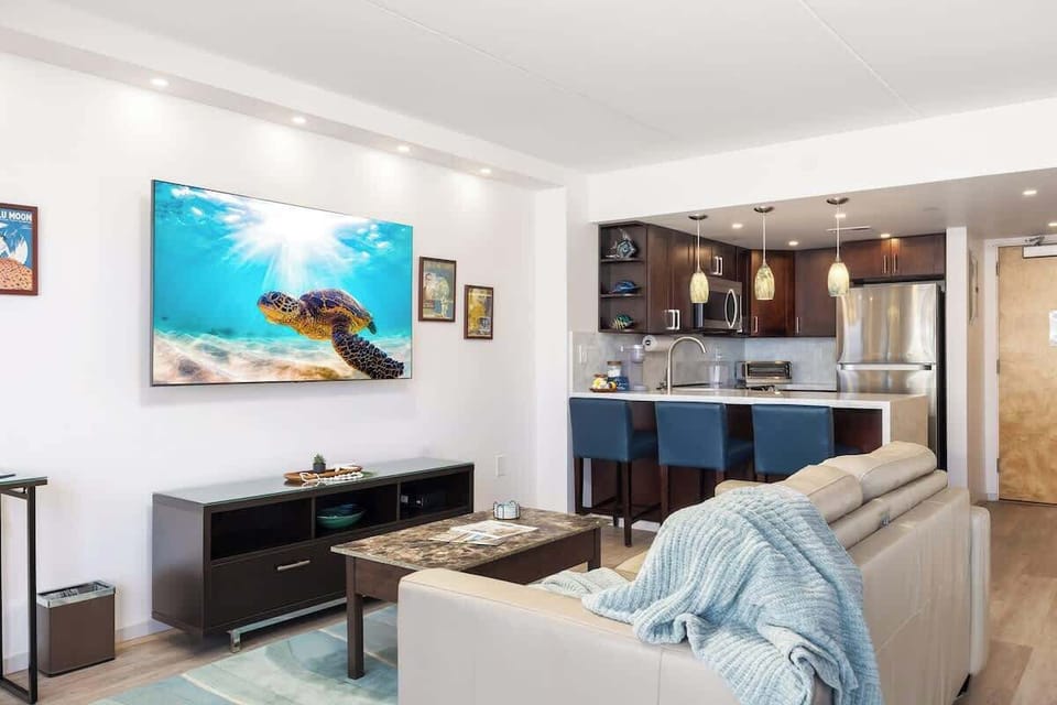 Your sleek, modern studio apartment features a full kitchen with bar seating, a sleeper sofa, a 65" smart TV, and a king-size bed.