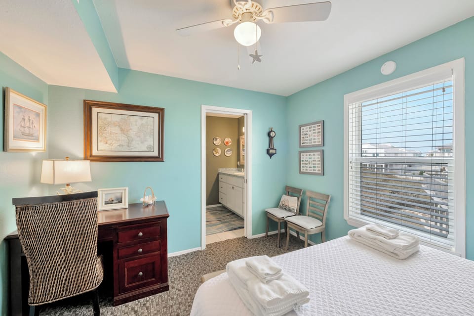 Unwind in your coastal-themed bedroom with soft blue walls, nautical art, and a comfortable workspace overlooking the surrounding area.