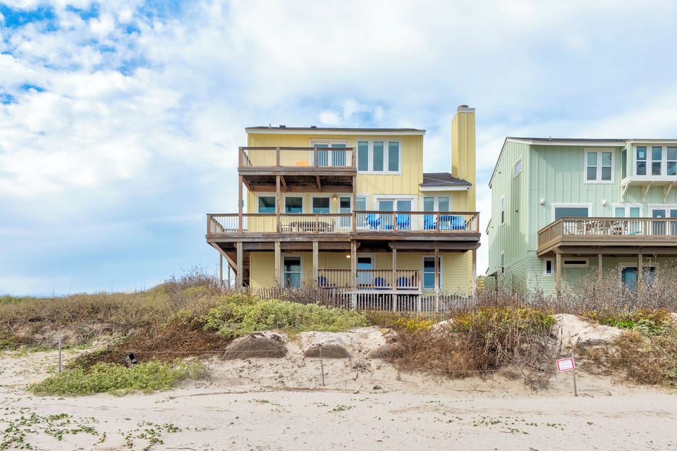 Oceanfront vacation home with multiple decks and direct beach access, nestled in coastal dunes under expansive skies.