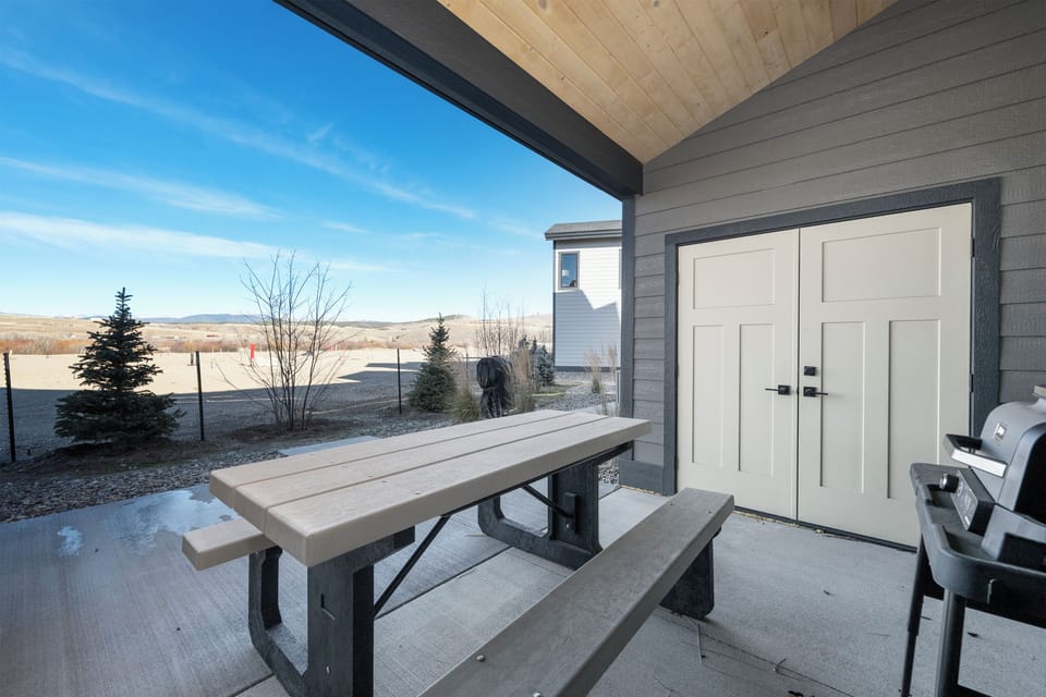 Your covered patio invites outdoor dining with a rustic picnic table and grill, perfect for prairie sunset barbecues.