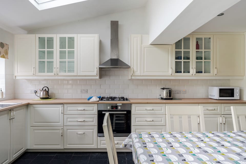 A bright, spacious kitchen with ample counter space, cabinet lighting, dishwasher, etc, and all essentials. Features a six-seater dining table, two-seater sofa, and double doors opening to the large garden—perfect for cooking, dining, and relaxing.
